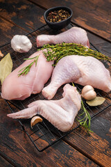 Raw chicken cuts (breast, leg, wing) on a rack with thyme, rosemary, garlic, and peppercorns on dark rustic wood. Ready for seasoning. © Mironov