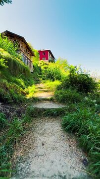 4K Vertical POV shot of a person walking on old stairs with grass growing on them in front of old wooden houses at Chehni Kothi in Kullu district, Himachal Pradesh, India. Tourist exploring hidden gem