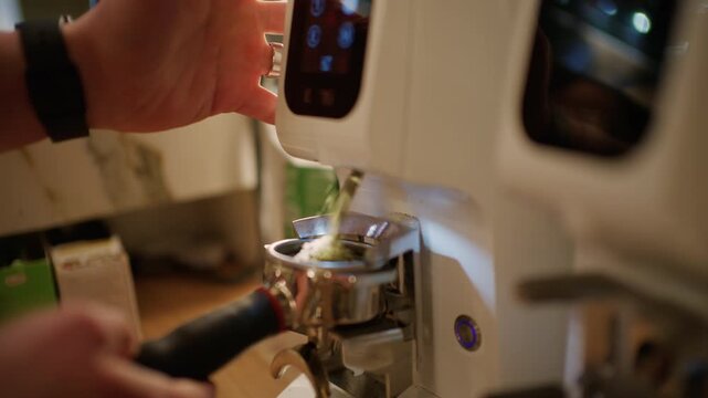 Close up of a barista using a white espresso machine as ground coffee or hot water flows into a metal portafilter