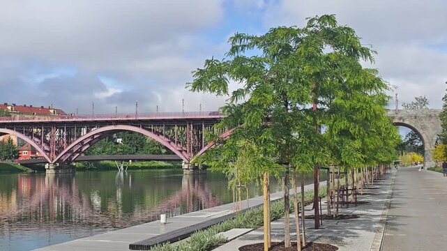 Green Embankment and Stari Most Bridge in Maribor city, Slovenia. Modern urban embankment with young green trees along the Drava river in Maribor. 