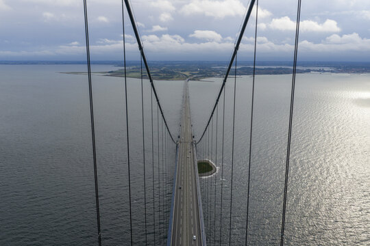 Aerial view of the Great Belt Bridge with its massive suspension cables stretching over the sea towards the horizon under a cloudy sky Denmark.