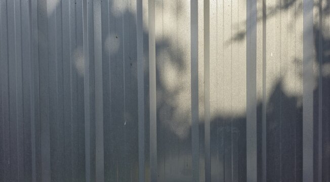 Tree shadow on corrugated galvanized iron sheet. Natural tree shadows cast on silver corrugated metal surface. High quality texture background of glossy zinc wall with shadows.