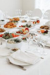 Fototapeta premium Vertical perspective looking down a long, elegantly served banquet table filled with glassware, white plates, and festive cold snacks.