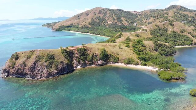 Aerial view of the northern headland near Labuan Bajo in Komodo National Park, Indonesia, surrounded by vibrant coral reefs and turquoise tropical waters under a sunny blue sky