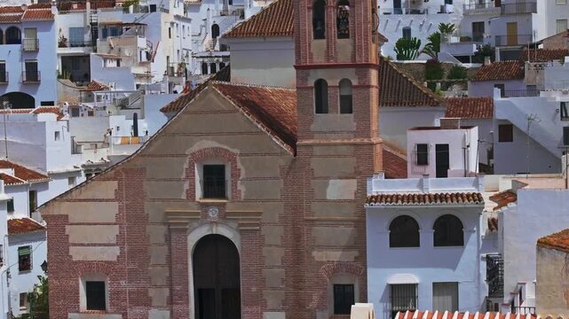 Drone footage of Frigiliana, Andalusia, Spain, showing a rising aerial view of a church tower surrounded by whitewashed hillside homes and mountain scenery.