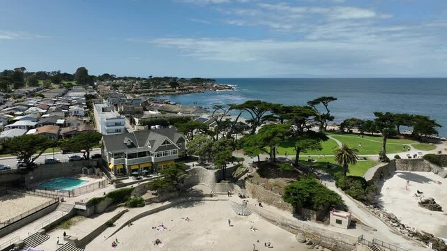 Cinematic aerial drone footage of Lovers Point Park in Pacific Grove, CA, showcasing sandy beaches, rocky shoreline, turquoise Pacific Ocean water, coastal roads, oceanfront homes, Monterey Bay