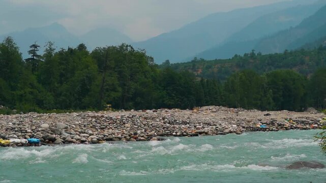 4K shot of flowing Beas river with beautiful mountain range and clouds in sky during evening  at Manali, Himachal Pradesh, India. Wild mountain river water in summer day. Tranquil natural landscape.