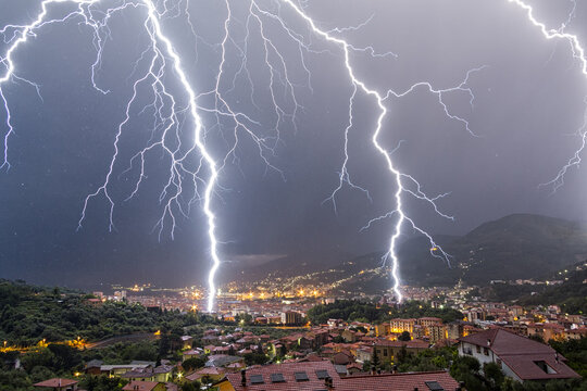 View of powerful lightning bolts striking over the city skyline and rooftops at night in La Spezia, Liguria, Italy.