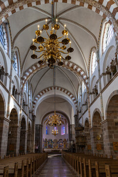View of the interior of Ribe Cathedral featuring Romanesque arches, vaulted ceilings, and ornate golden chandeliers hanging above wooden pews in Ribe, Denmark.
