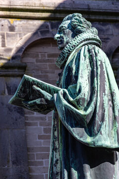 View of the Hans Tausen statue holding a book in front of the historic Ribe Cathedral with its stone arches and weathered walls in Ribe, Denmark.
