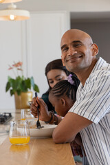 Diverse family sitting on kitchen island, man holding fork near bowl, orange juice, copy space © wavebreak3