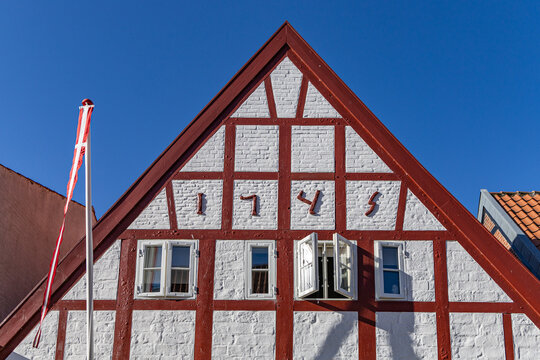View of a traditional half-timbered house gable with red beams and white brickwork under a clear blue sky in Ribe, Denmark.