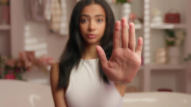 Latina American woman showing stop gesture looking at camera in glamour bath Hispanic female rejecting show limit sign with palm ethnic girl refusing in pink bathroom beauty procedure cosmetic problem