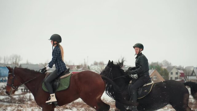 Caucasian duo riding tandem horses on snowy field learning equestrian skills, female student and male instructor in helmets, green saddles and bridles, village houses in background, calm education