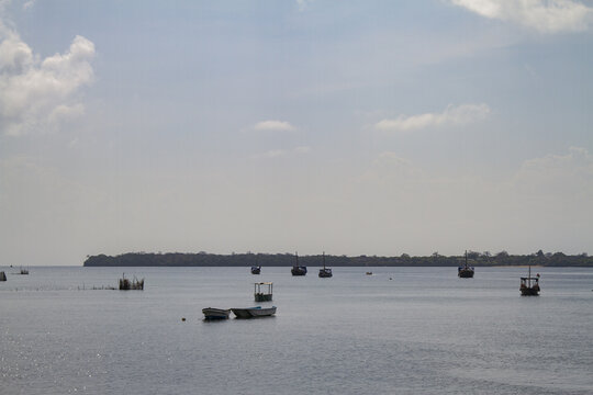 View of Tiwi Beach with traditional wooden boats anchored in the calm waters near the distant coastline under a bright sky Tiwi, Wilaya ya Kwale, Kenya.