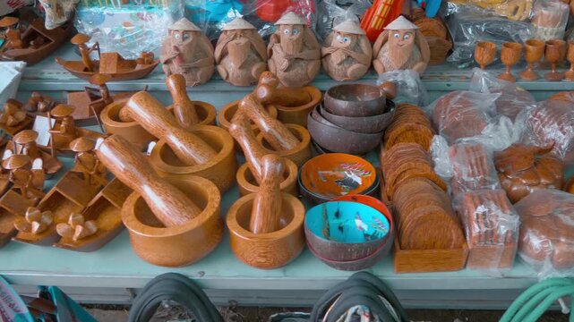 Crafts made of wood and coconut are sold at a street vendor's stall. Skillfully crafted mortars and pestles, bowls, figurines of a boatman with an oar wearing a Vietnamese Non La hat, and amusing monk