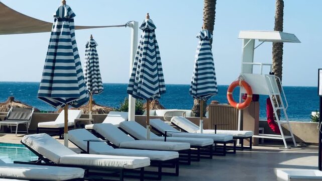 Luxury 5-star hotel resort pool area with striped umbrellas and lifeguards tower in Sharm El Sheikh. Beautiful sea view lounge terrace of premium all inclusive holiday destination in Egypt.