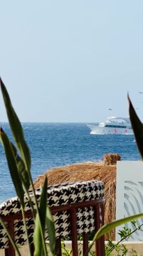 Luxury 5-star hotel resort outdoor terrace with houndstooth chairs and sea view in Sharm El Sheikh. Beautiful white yacht in Red Sea background of premium all inclusive holiday destination in Egypt.