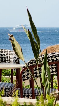 Luxury 5-star hotel resort outdoor terrace with houndstooth chairs and sea view in Sharm El Sheikh. Beautiful white yacht in Red Sea background of premium all inclusive holiday destination in Egypt.