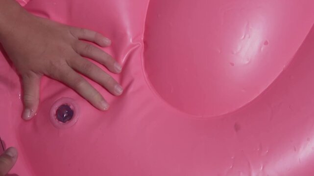 Close up of a child hands opening the air valve on a pink inflatable pool float to deflate