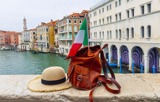 leather backpack with italian flag and straw hat on a bridge over the grand canal in venice, italy, summer travel concept