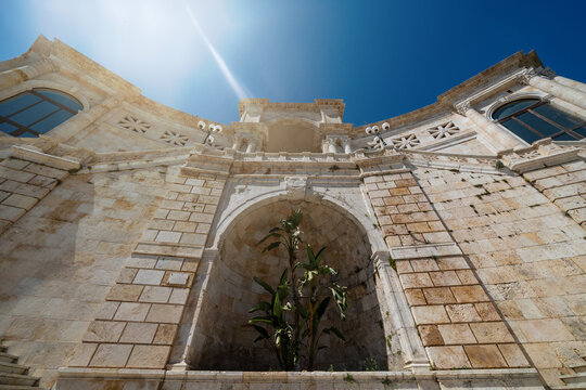 View of the Bastione di Saint Remy neoclassical stone facade with arches and columns under a bright sun flare and clear blue sky in Cagliari, Sardegna, Italy.