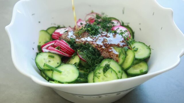 Close-up of preparing a simple summer salad by tossing sliced cucumbers and radishes with mustard dressing in a large salad bowl