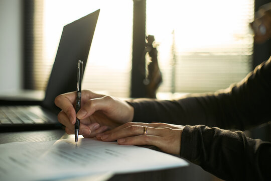 Close up of young adult woman signing divorce papers beside laptop, documenting legal separation and marital breakup. Useful for family law, mediation, custody, legal services marketing