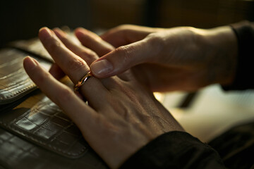 Fototapeta premium Close up of middle aged woman removing wedding ring from finger, signaling divorce, separation, breakup. Useful for legal services, counseling, family law marketing