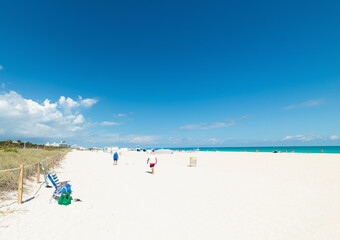 Fototapeta premium Beach chairs with beach bag and three men walking away on South Beach shoreline