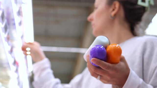 Young woman shopping for personal hygiene products in a store, carefully selecting an antiperspirant from the shelf while holding several other colorful bottles of deodorant
