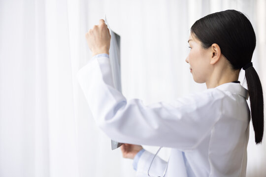 Asian Female Doctor in White Coat Reviewing X-ray Image