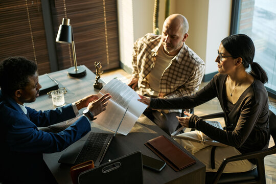 Black male lawyer reviewing documents with middle aged couple during divorce consultation in office. Legal dispute, custody, settlement, mediation marketing, high angle view