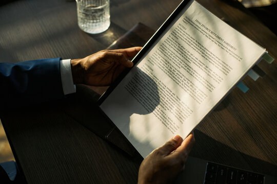 Close up of middle aged man holding divorce settlement agreement, reviewing legal paperwork during separation process. Useful for family law, mediation, custody, legal services marketing