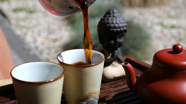Pouring aromatic black tea from a glass pitcher into ceramic cups during a traditional gongfu cha ceremony, a peaceful and mindful ritual celebrating the art of tea drinking in a zen garden