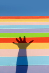 Obraz premium shadow on hand against colorful wooden fence. hand shadow, silhouette of palm on rainbow color striped background. conceptual minimal style photo representing fun, happiness, childhood, friendship