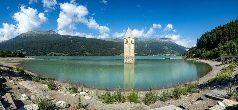 View of the historic submerged bell tower of Reschensee standing in the turquoise water surrounded by lush green mountains Graun im Vinschgau, Trentino-South Tyrol, Italy.