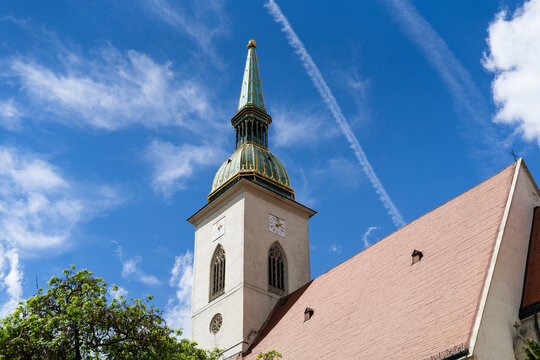 View of the historic St. Martin's Cathedral spire and tower under a bright blue sky with wispy clouds and a contrail Bratislava, Bratislava Region, Slovakia.