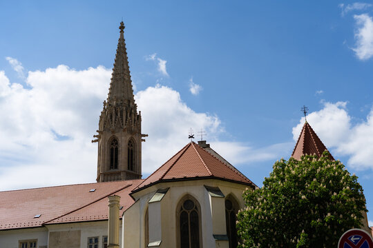 View of the historic Franciscan Church with its ornate Gothic spire and red-tiled roofs under a blue sky with white clouds in Bratislava, Bratislava Region, Slovakia.