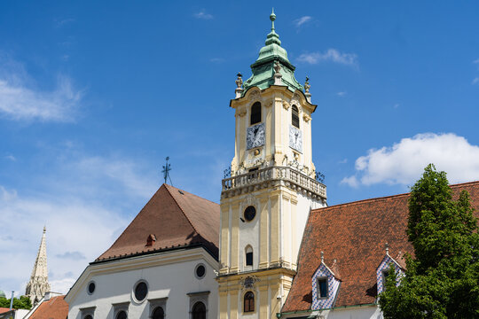 View of the Old Town Hall clock tower with its green baroque roof and historic white facade under a clear blue sky in Bratislava, Bratislava Region, Slovakia.