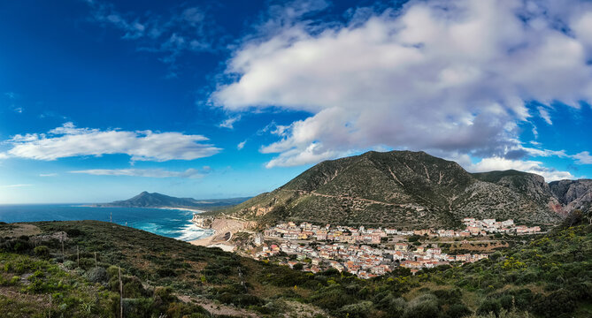View of the coastal village nestled at the foot of green mountains along the Mediterranean coastline Buggerru, Sardinia, Italy.