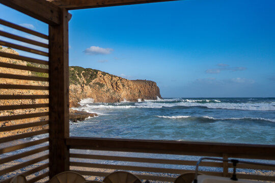 View of Spiaggia di Cala Domestica with waves crashing against the rugged cliffs under a clear blue sky in Provincia del Sulcis Iglesiente, Sardegna, Italy.