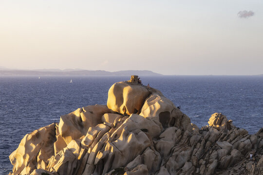 View of the unique granite rock formations of Capo Testa with people standing on the peaks overlooking the blue Mediterranean sea during sunset Capo Testa, Sardegna, Italy.