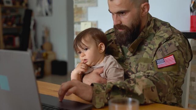 American male soldier with baby son working on laptop at home - Homecoming, military uniform and family concept
