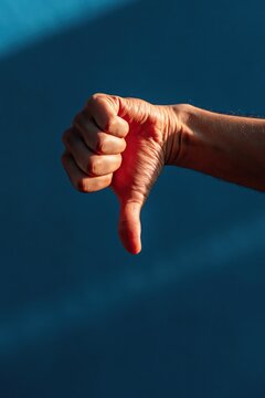 Hand showing thumbs down against teal background with side light