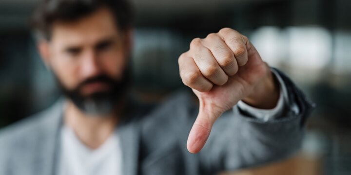 Bearded man delivering thumbs down gesture in modern workplace environment