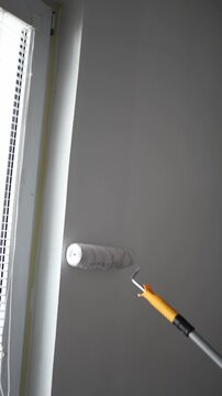 Vertical screen Paint roller applying fresh white coating near window frame during apartment renovation and interior wall restoration in modern bright living space