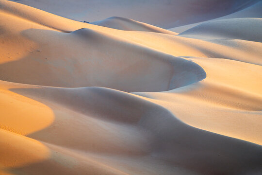 View of Eastern Sands featuring rolling sand dunes with soft golden light and deep shadows at sunset Oman.