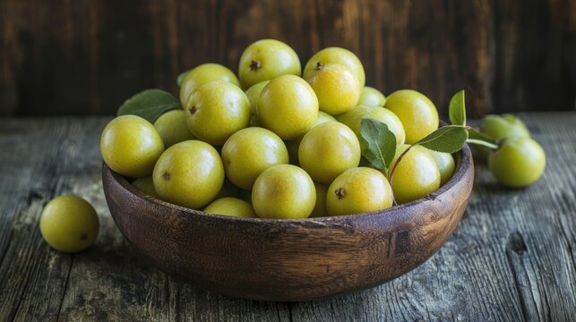 A rustic wooden bowl filled with freshly picked greenish-yellow greengage fruits resting on a farmhouse table