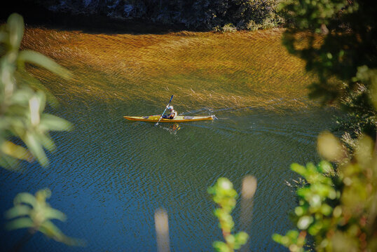 View of a person paddling a yellow kayak on the clear waters of Nahuel Huapi Lake framed by green foliage in San Carlos de Bariloche, Rio Negro, Argentina.